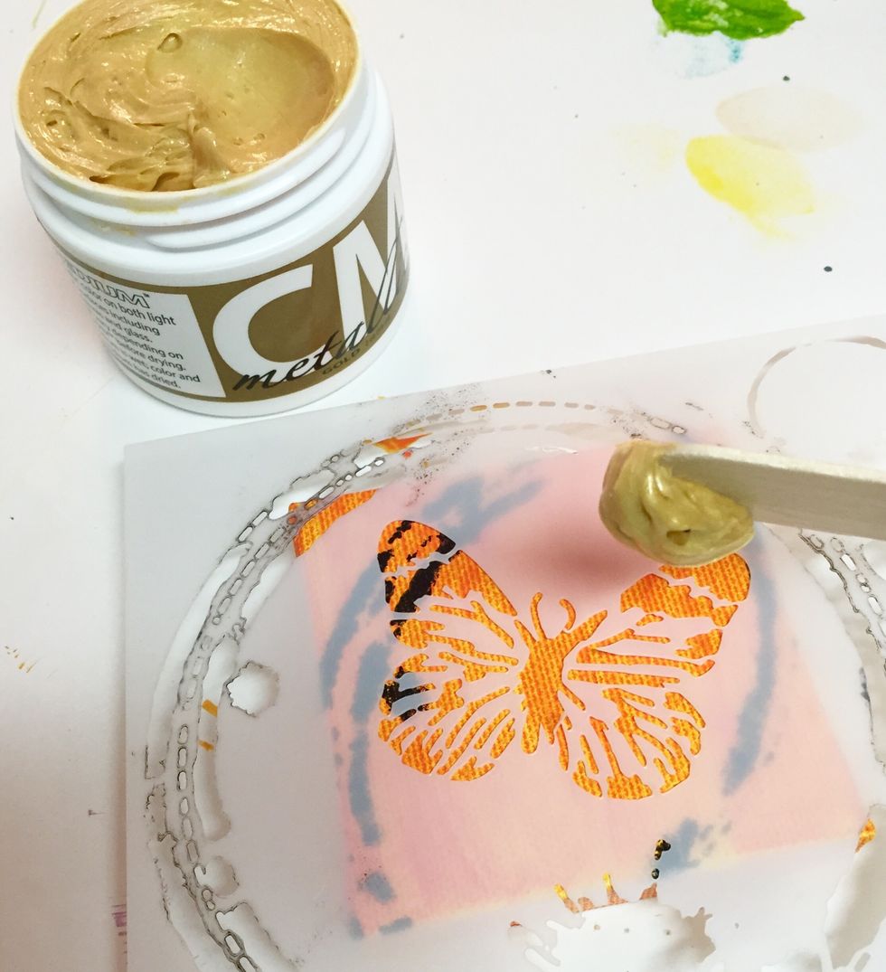 use palette knife or craft stick to apply Gold CM Metallic over butterfly portion of MINI BUTTERFLY COLLAGE stencil on orange mini canvas. be sure to use LOTS of medium, you can return excess to jar.