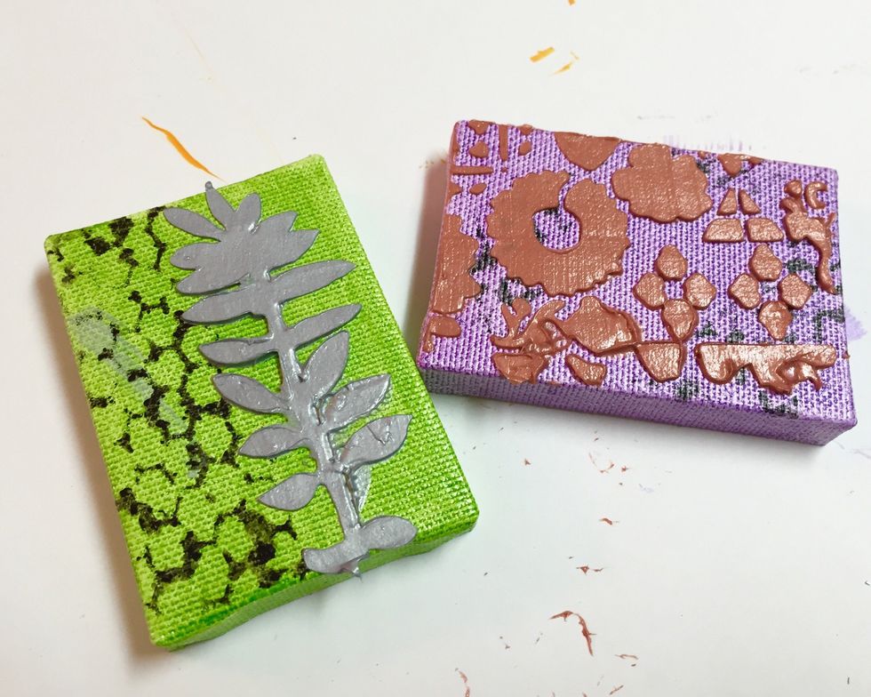 use Silver CM Metallic to add design from MINI HERBARIUM stencil to lime canvas and Copper CM Metallic to add design to purple canvas using MINI POSTCARD stencil. let dry.