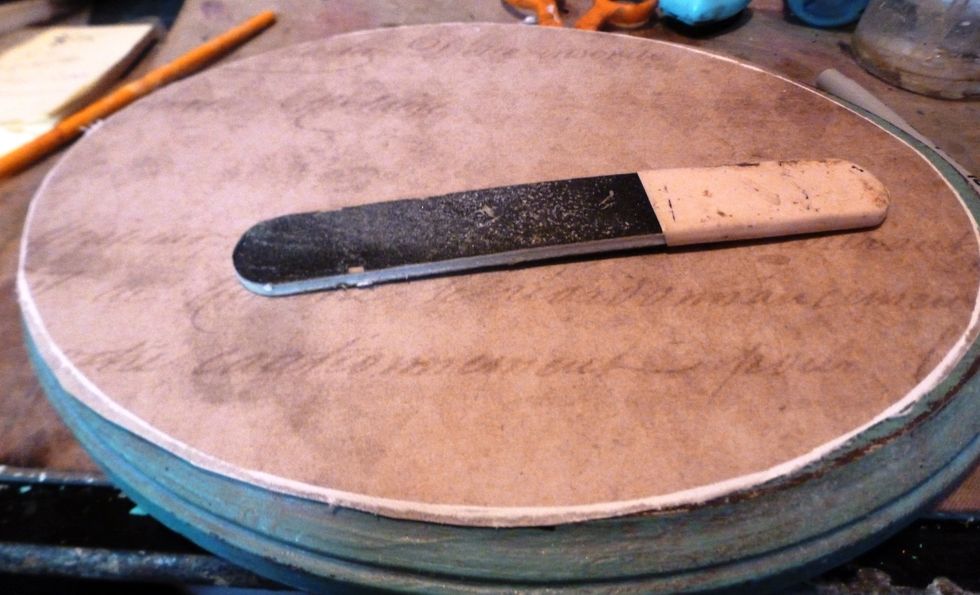 Use the emery board to file around the edges of the plaque. It will create a white boarder. You can use this as a guide to trim off the excess paper. Then repeat to make it smooth.