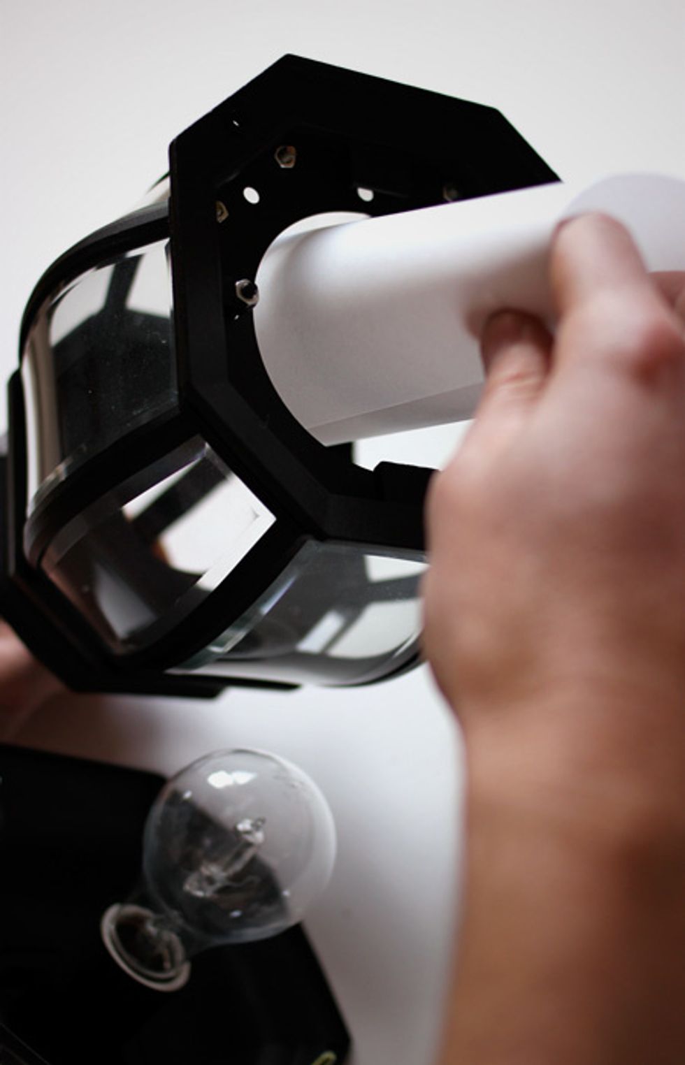 Use the natural curl of the paper to help wrap the rectangle into a cylinder around the lightbulb. This will diffuse the harsh light of the outdoor lamp for indoor use.
