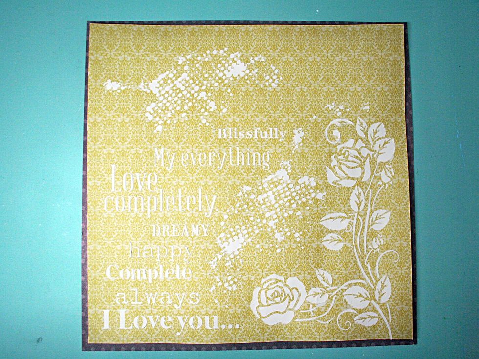 Use the Prima Floral Rose stencil and white 13 Arts Ayeeda Gesso to mask a design onto the yellow print paper, Zest.  Allow that to dry and they adhere to the brown frame.