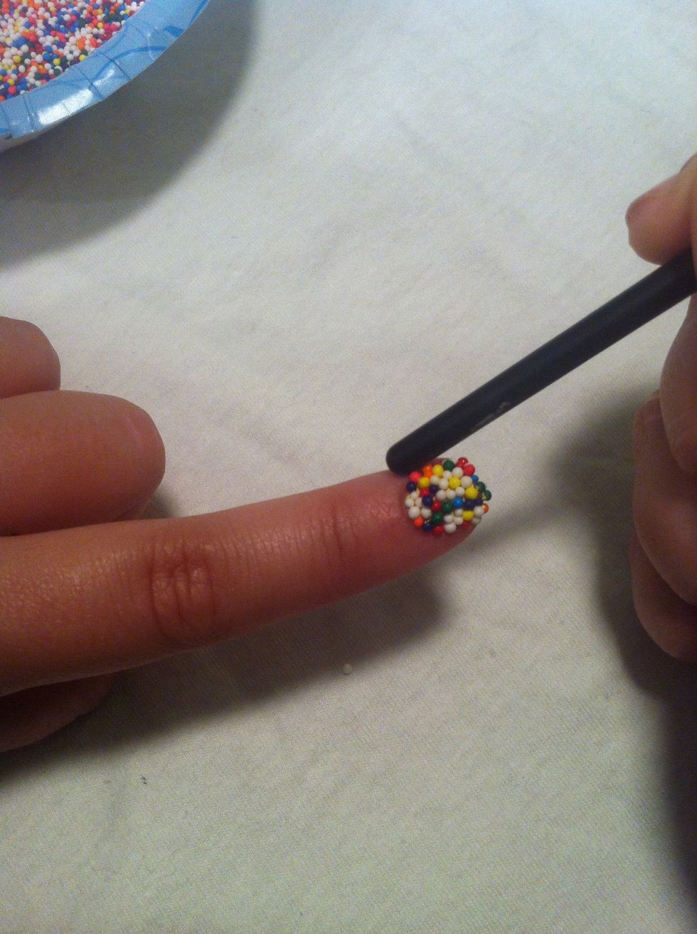 Use the stick to push the sprinkles from the cuticle to the nail bed. Be patient and don't be too rough, the sprinkles can still slide a bit. Clean off the end of the stick if it gets sticky.