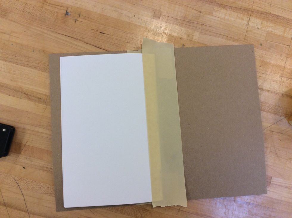 Use the tape in the center, going from top to bottom, and covering from 1/4 to 1/2 inch of the paper booklet. Then, use the scissors to cut off the extra tape at the top and bottom of your booklet.