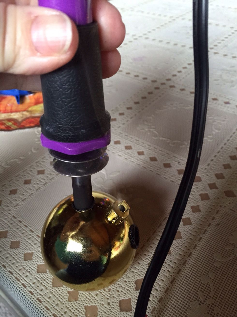 Use the wood burner to carefully burn two holes at the top of the larger ornament, which will be the head. Make it big enough to fit the top piece of the smaller ornaments.