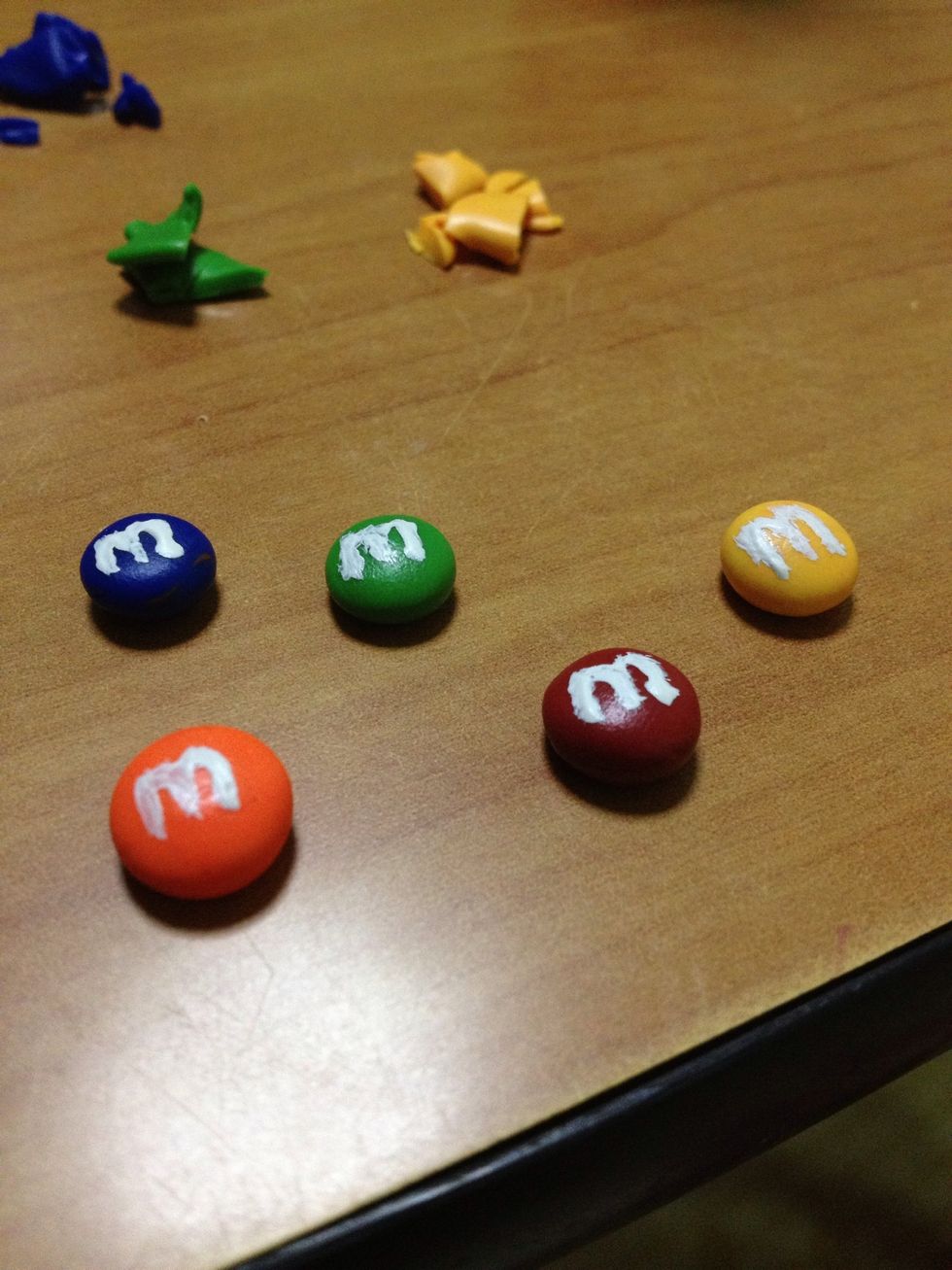 Use white acrylic paint and a toothpick to write an 'M' on your polymer clay M&Ms. Remember to do so for the other side.