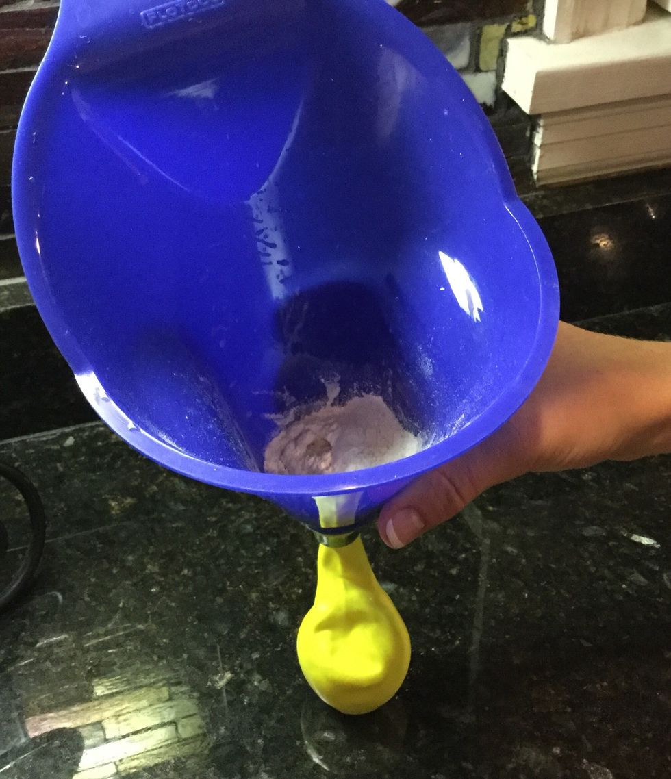 Use your spoon to scoop the flour and place it inside the funnel. Use the pen to push the flour inside of the balloon or shake the funnel.
