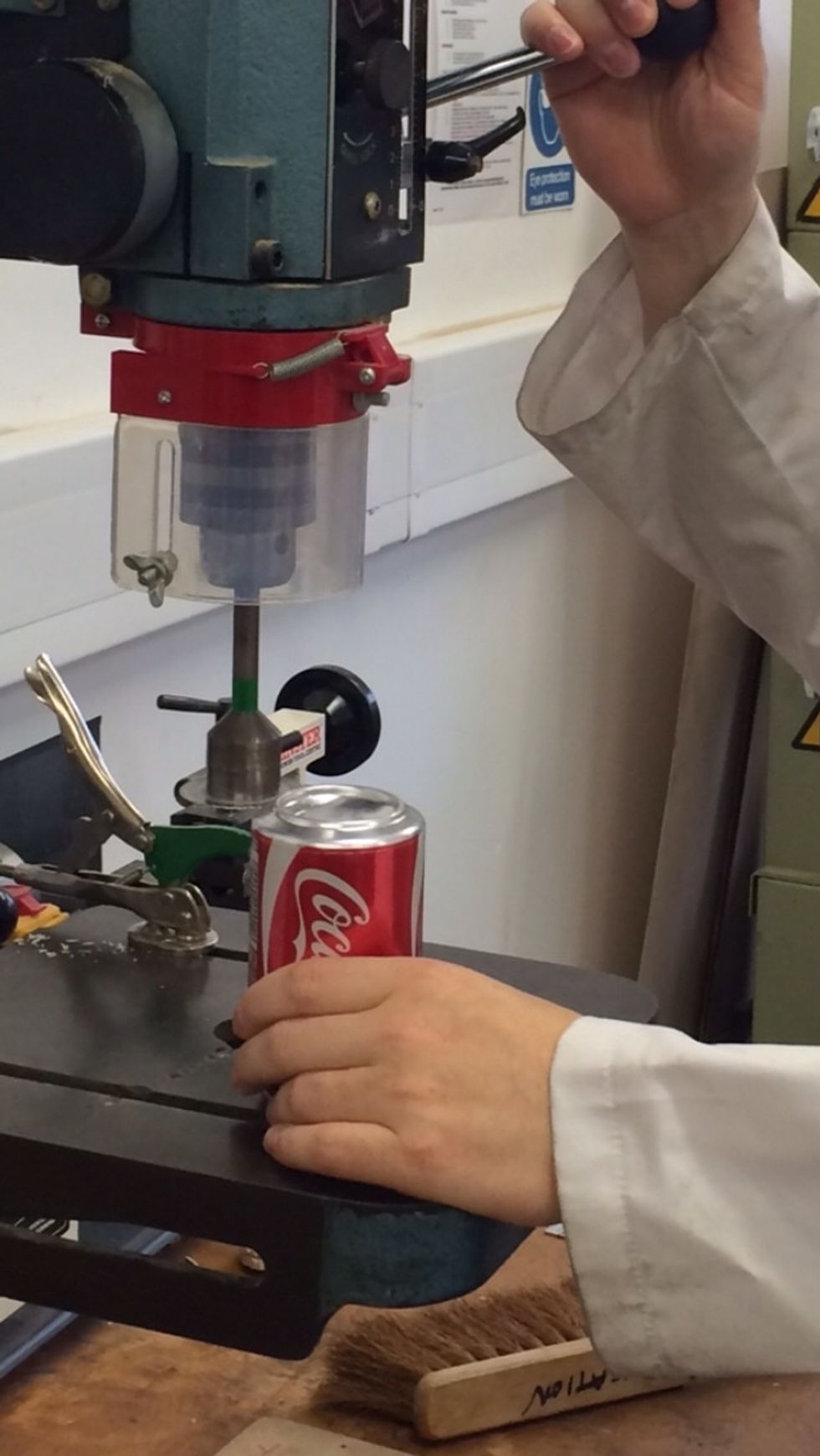 Using a diamond cutter on a pillar drill. Carefully cut the bottom out of the can.  Male sure you allow a small amount of the can wall to remain attached to the bottom of the can.