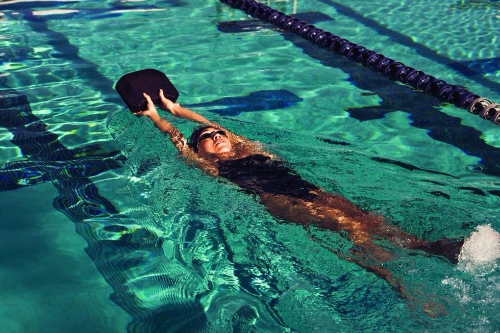 Using a kickboard, lay on your back holding the kickboard. Kick your legs up and down. Keeping your toes pointed and legs straight. This is known as backstroke kick.