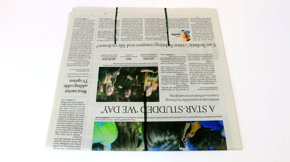 Using a marker, draw two lines at the top of the page and one near the bottom at the center, each about 4" long. See the black lines drawn on the newspaper above for reference.