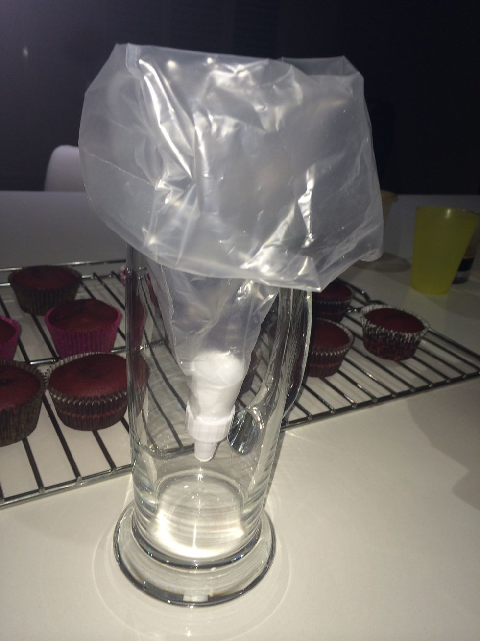 Using a piping bag or disposable piping bag place it into cup so you can fold the edges over and easily spoon in the frosting