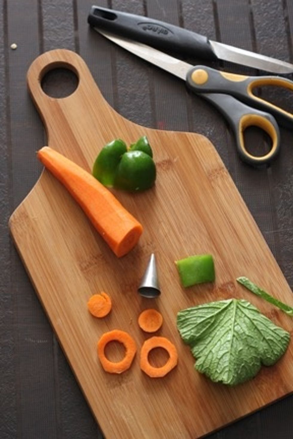 Using a piping tip or bottle cap cut out small circles from 2carrot slices ,keep the rings aside. Cut a small square from green capsicum .Slightly trim the edges of the radish green into thin strips.