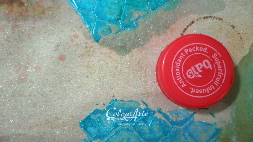 Using a plastic bottle cap, add circles of color using ColourArte Nutmeg Radiant Rain Color Concentrate. I applied some of the color to my craft mat and picked up the color on the cap.