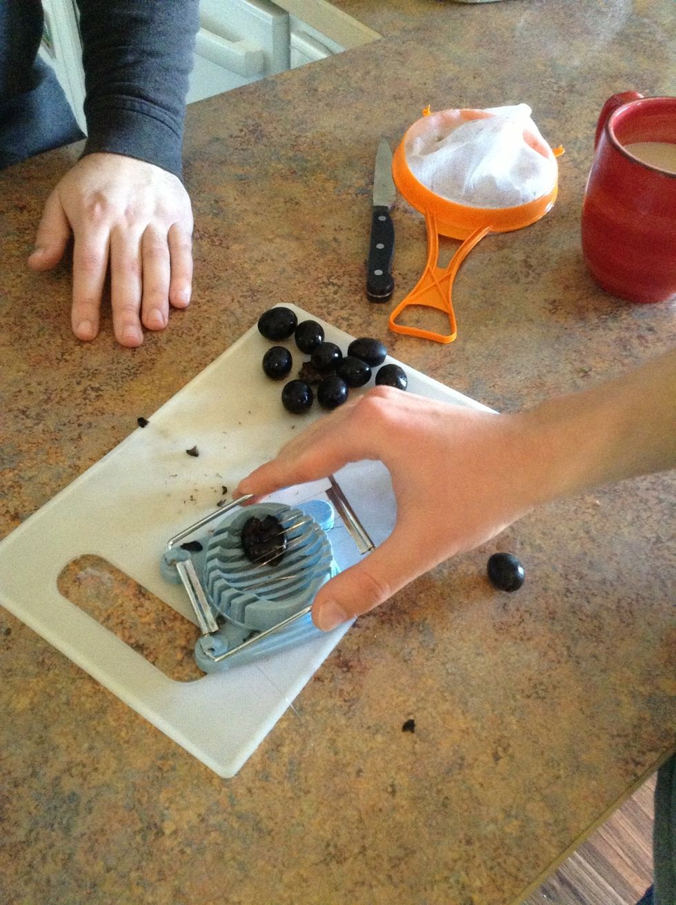 Using an egg slicer put 1 olive at a time into the base and press the handle down. This will slice the olives