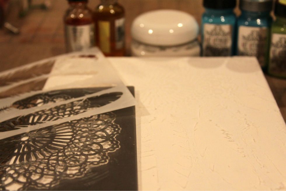 Using Art Anthology Mud and stencils, spread mud through stencils onto canvas and let dry. Apply Gesso to whole canvas.