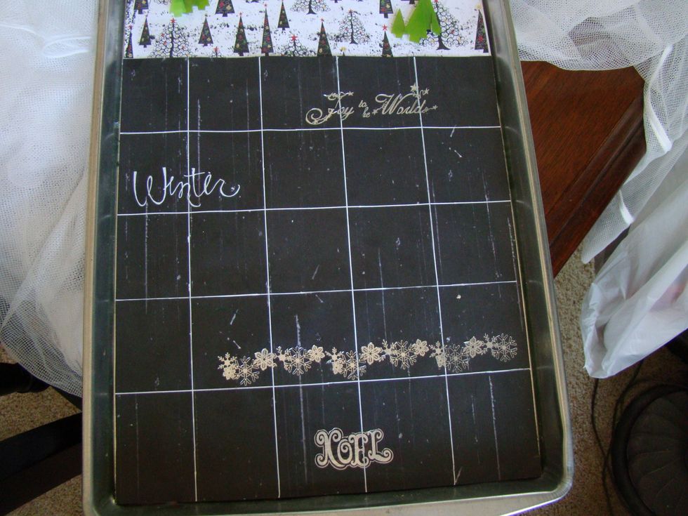 Using chalkboard paint I covered the remaining portion of the cookie sheet. Using a white pen I drew out the grid lines. I randomly applied chalkboard Christmas rub ons here and there.