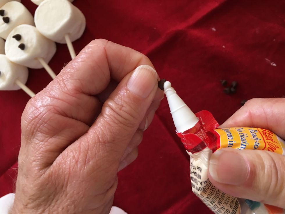 Using cookie icing (sold ready to use in grocery stores) you put a small blob of icing on the mini chip then set on the marshmallow.