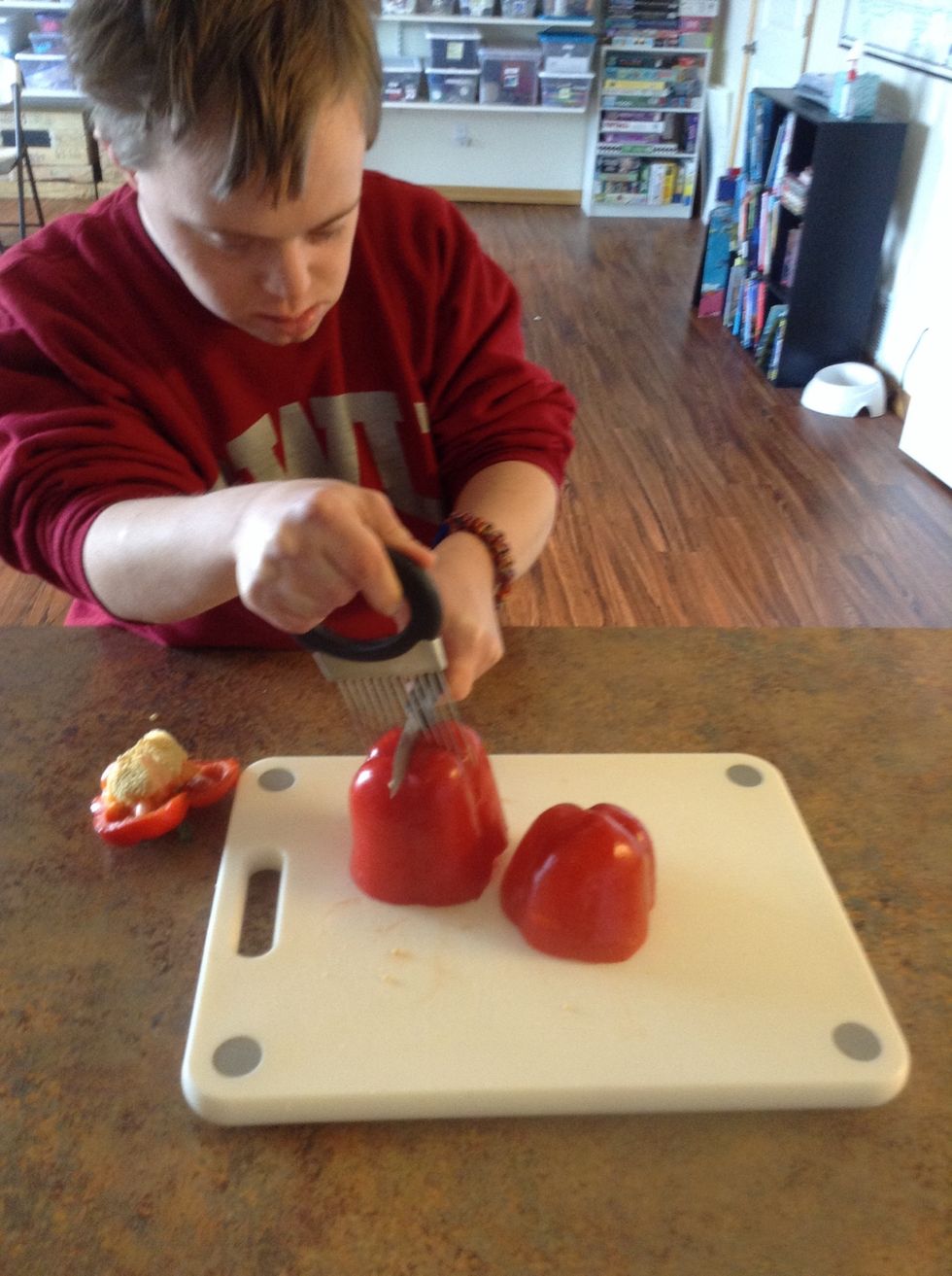 Using cutting board, knife, and cutting guide cut the red peppers in half