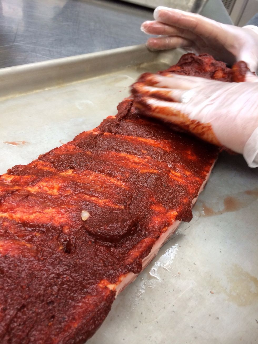 Using gloved hand evenly spread wet rub over ribs.