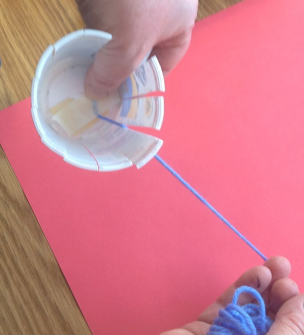 Using masking tape, attach the end of your yarn to the base inside the cup and lead the ball to the outside through one of the spaces between the warps.