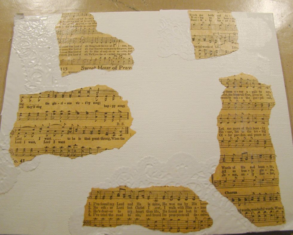 Using Mod Podge apply doilies to edges of canvas. Tear pieces of sheet music and adhere to canvas.