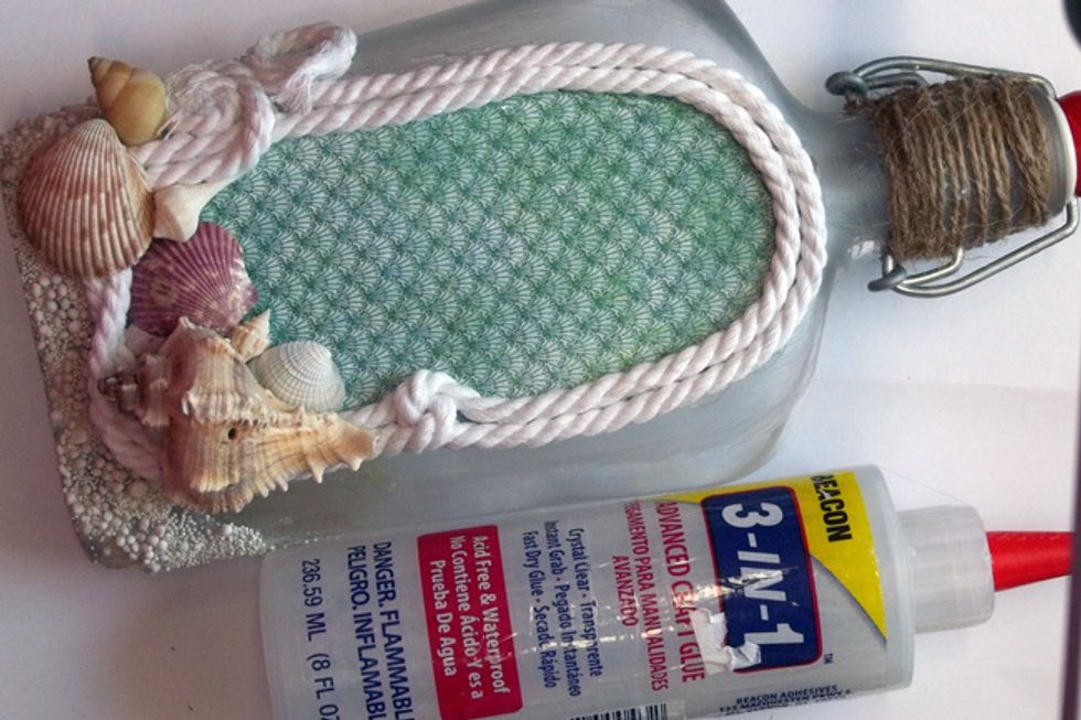 Using strong glue, add rope trim around the edge of the fussy-cut image and glue shells along the bottom of the bottle.