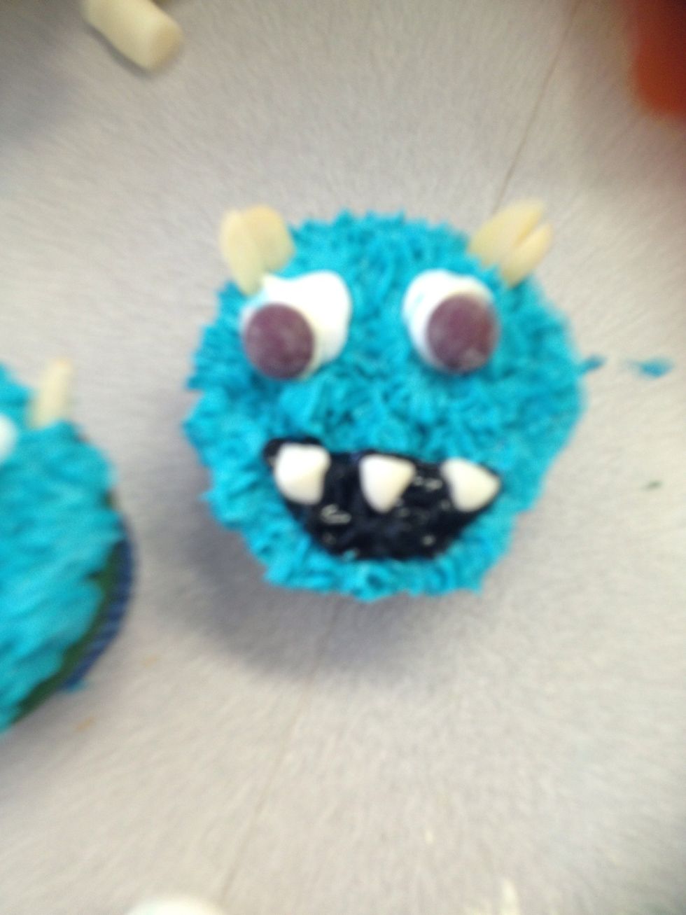 Using the black icing writing to draw a mouth and cut the corners of each milk bottle to make teeth