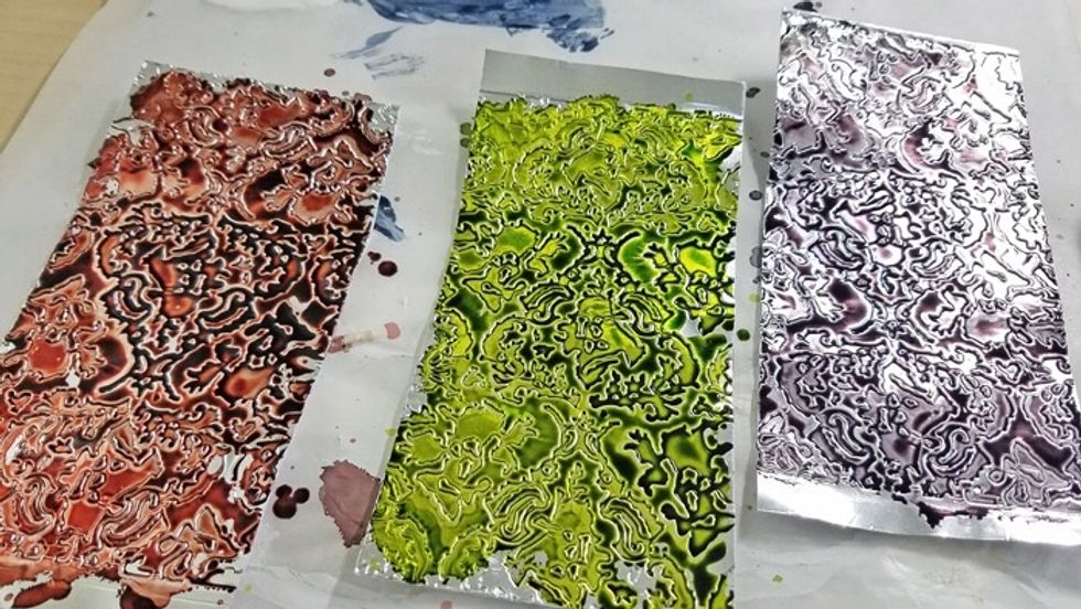 Using three different colors of alcohol ink, color each embossed metal sheet.