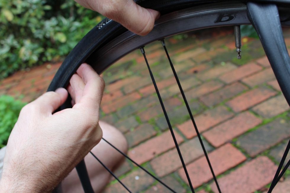 Using your fingers, begin to press the tire back under the rim while being careful to avoid pinching the new tube between the wheel's rim and the tire. (The newer the tire, the harder this is.)