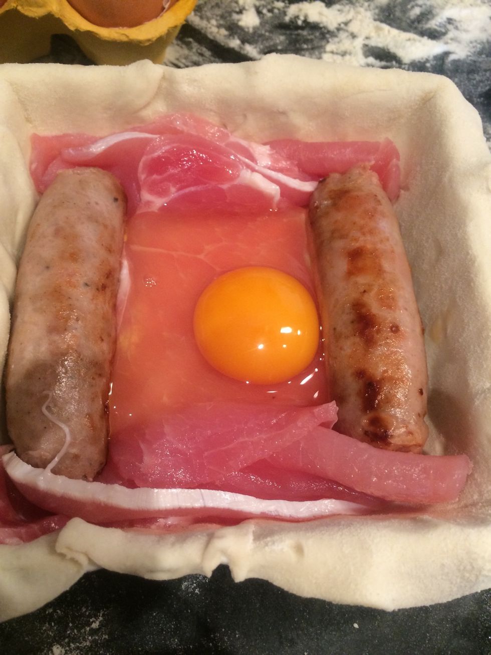 Using your sausages and bacon (which is raw), make a little "dam" for your egg/s. If you're making one big pie, twist the bacon and use it to make dividing "walls" between the eggs or use sausages.