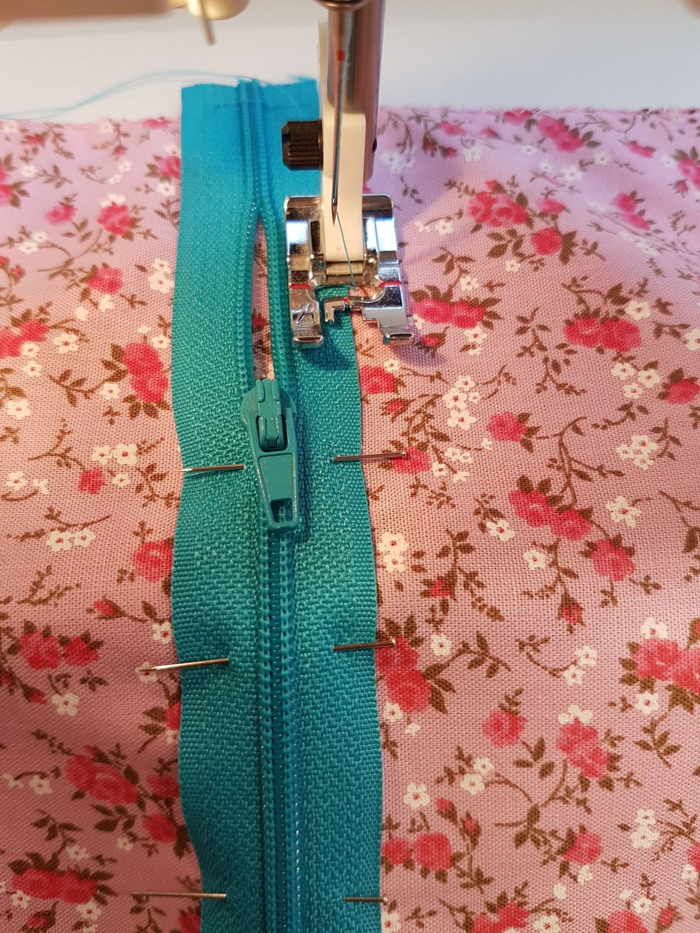 V\u00e4lj en tr\u00e5d som passar dragkedjan. Sy fyra g\u00e5nger fram och tillbaka med zickzack (s\u00f6m nr 5) p\u00e5 b\u00e5da sidorna av dragkedjan. Den r\u00f6da mittmarkeringen p\u00e5 pressarfoten ska f\u00f6lja kanten p\u00e5 dragkedjan.