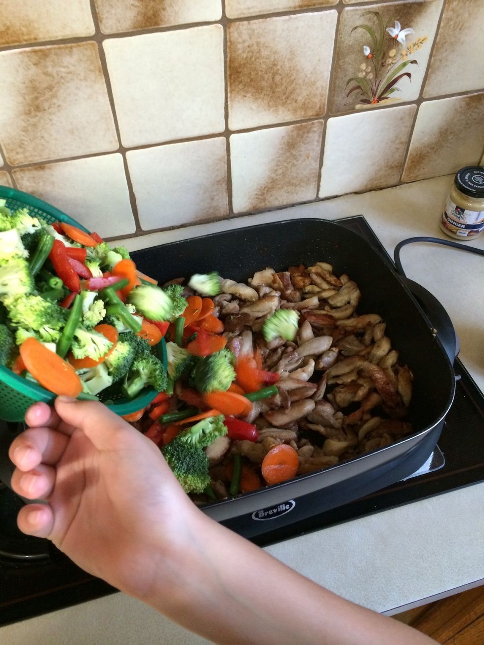 Wait for the chicken to brown, when it does add the vegetables and 1/3 Hoi Sin sauce bottle and stir. Put the lid on and let it cook for 5 minutes.