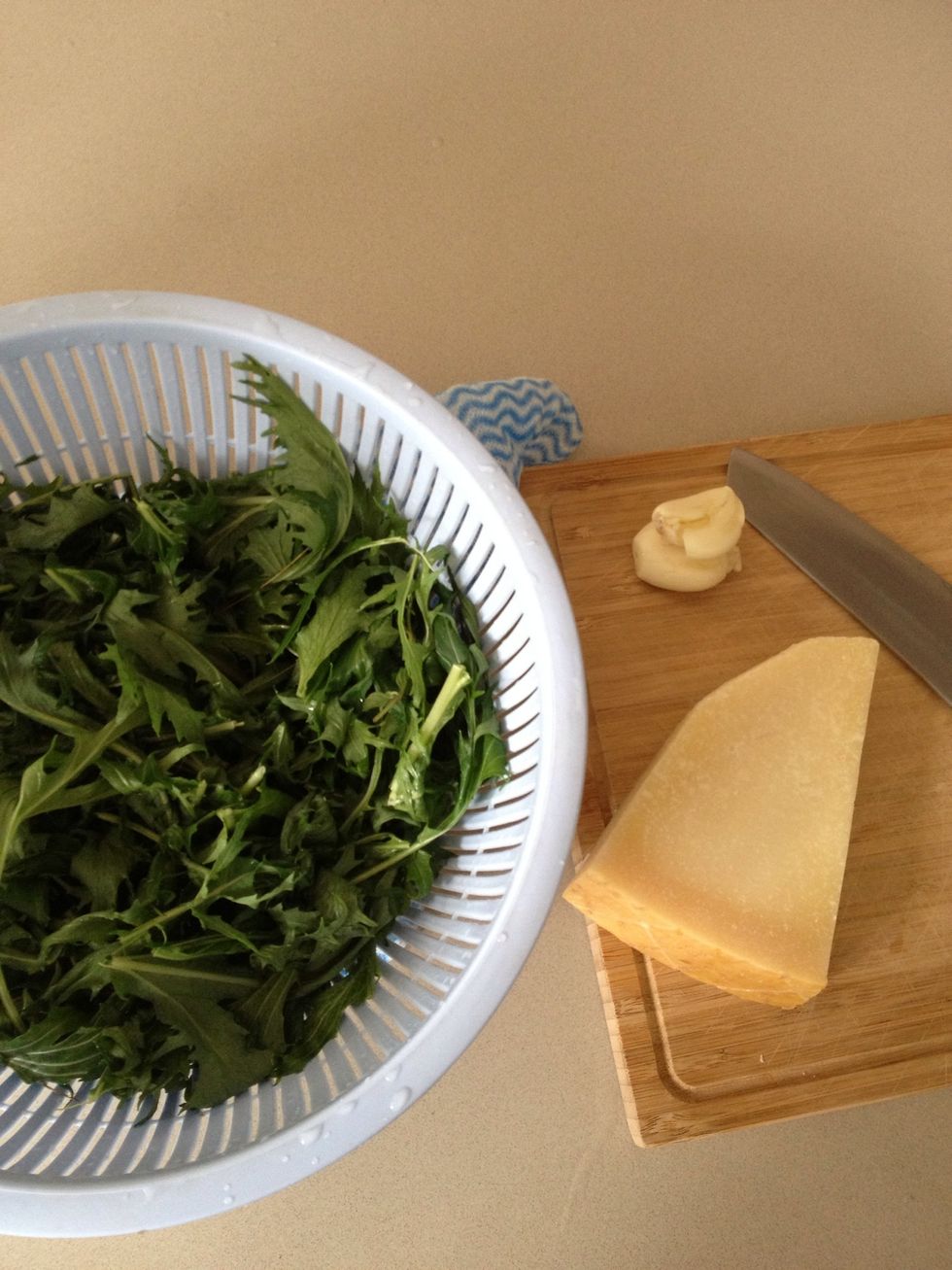 Wash mizuna leaves (rocket can also be used). Smash and peel garlic clove. Chop Parmesan cheese into rough squares of 2cm .
