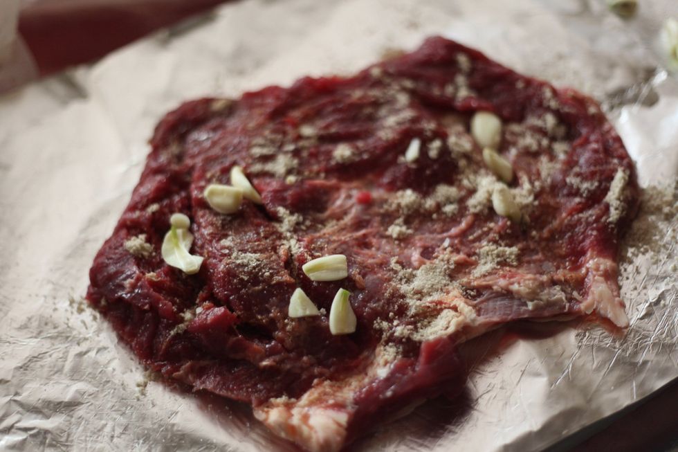 Wash your hands, spread the stock powder first onto only one side of the meat. Wherever you have tenderized, put some garlic in the crevices. And push down.