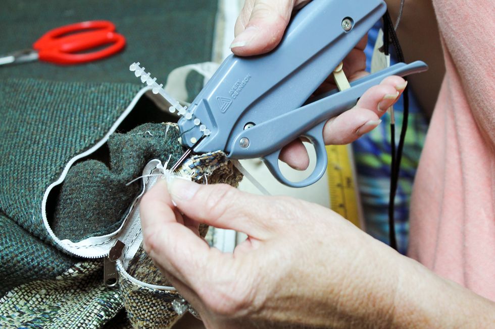 We use our tack gun and shoot two tacks into the end of the zipper but you could also use a hot glue gun  to dab a little dot on the front side and back side of the zipper just below the slide.