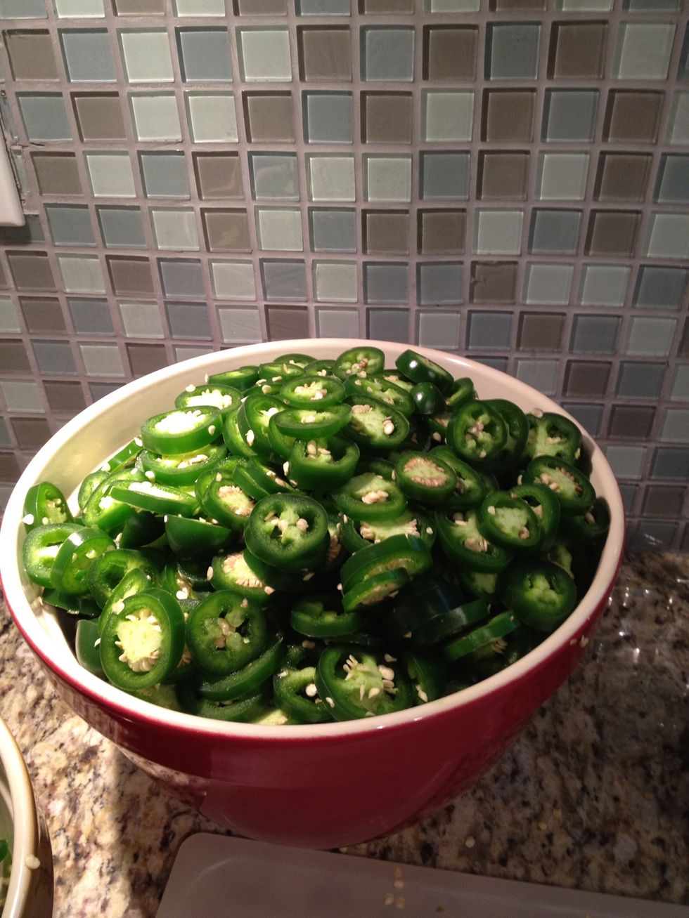 Wearing latex gloves, remove the stems from the jalape\u00f1os with a knife and discard, and slice the jalapenos into 1/8 inch round discs.