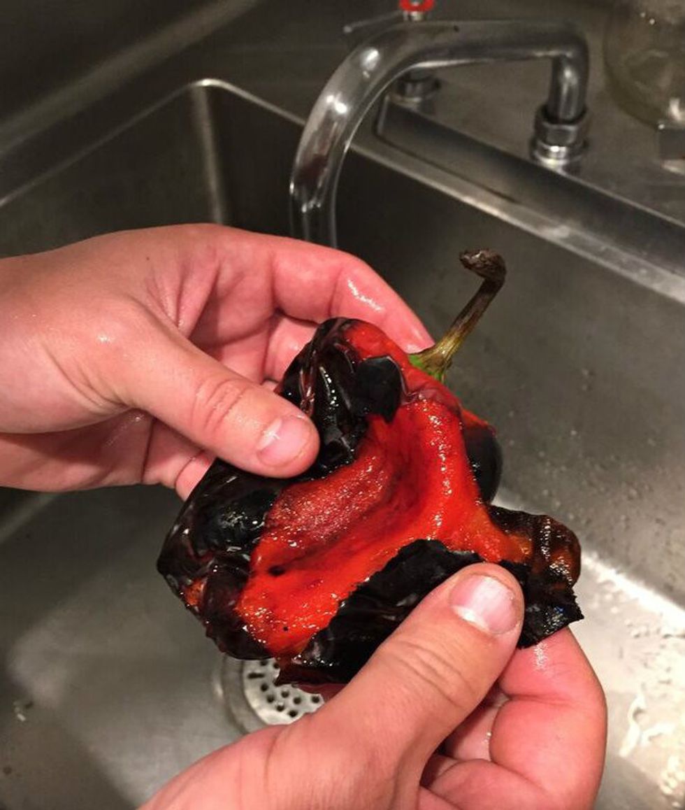 Wet your hands and begin to remove the skins from the peppers, along with the stem and seeds.