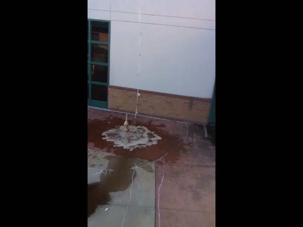 When the geyser has finished erupting, one lab member with safety goggles on, picks up bottle of Diet Coke