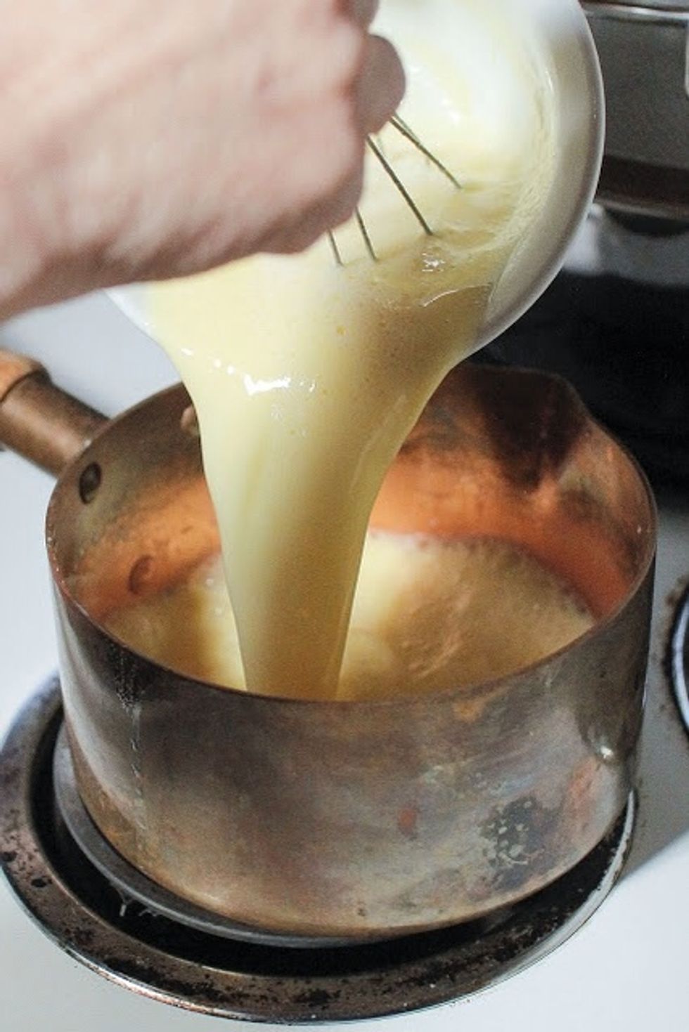 When the milk, sugar, and salt mixture is warm, pour it into the bowl of egg yolks. Pour it in slowly and keep whisking . Pour the egg yolk, milk, sugar, and salt mixture back into the pot.