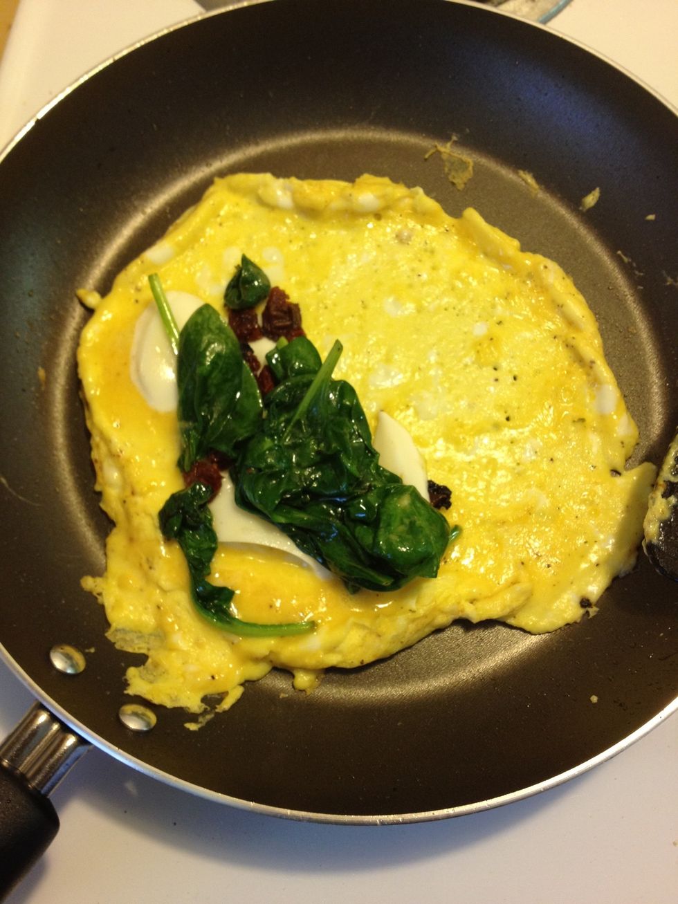 When the mozzarella is starting to melt, add the spinach, garlic, and sun-dried tomatoes on top of the cheese and fold the omelet.