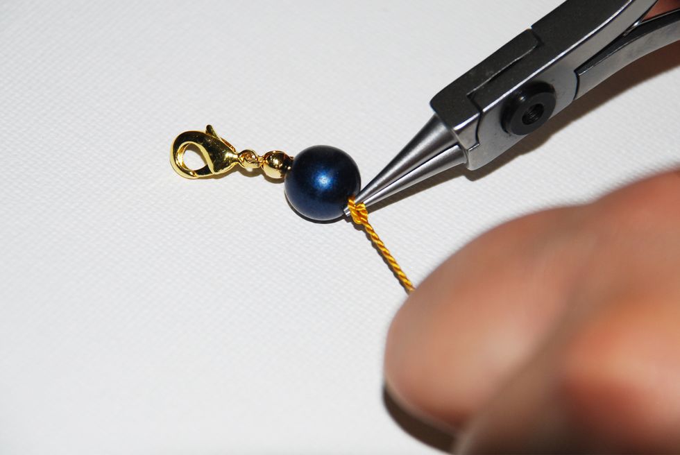 When your knot is as tight as it can be over the tip of the pliers, gently slide out the tool, and pull the long thread to tighten the knot even closer to the stone.