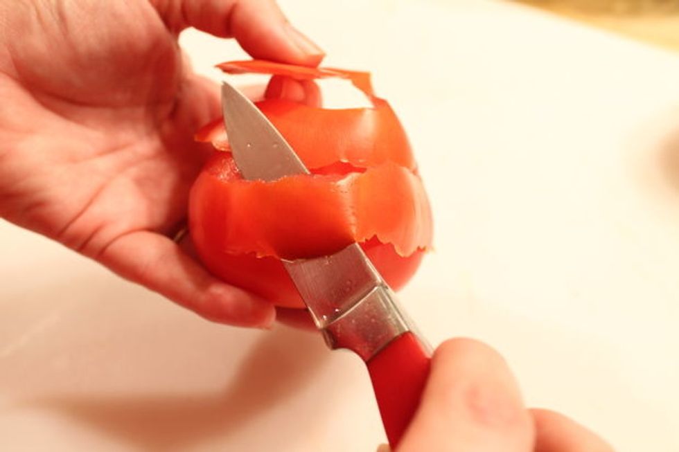 While cutting, slowly turn the tomato and without detaching the base, begin peeling the tomato in a single strip, about 1/2" wide, in the same manner you would peel an apple.