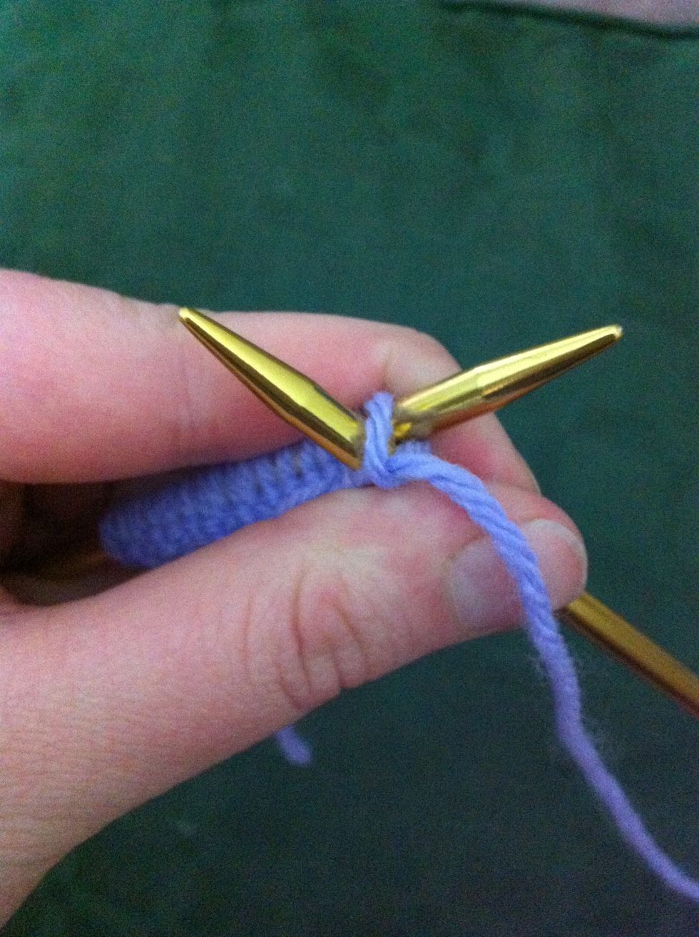 While holding working yarn in right hand pull right needle down through cast-on stitch catching the working yarn and pulling it through the stitch on the left needle.