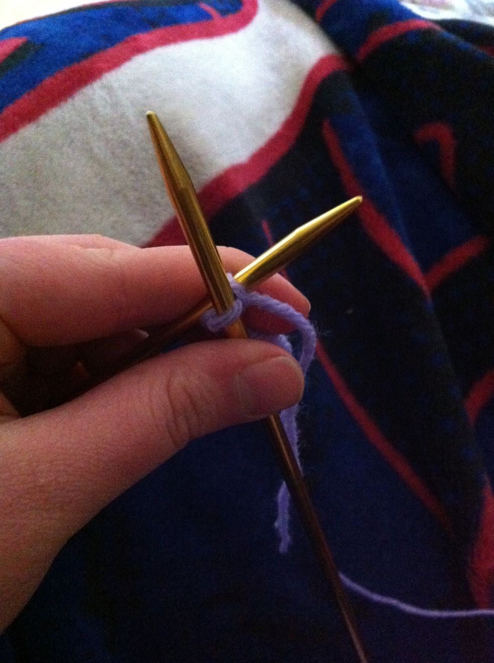 While holding working yarn in right hand pull right needle down through cast-on stitch catching the working yarn and pulling it through the stitch on the left needle.
