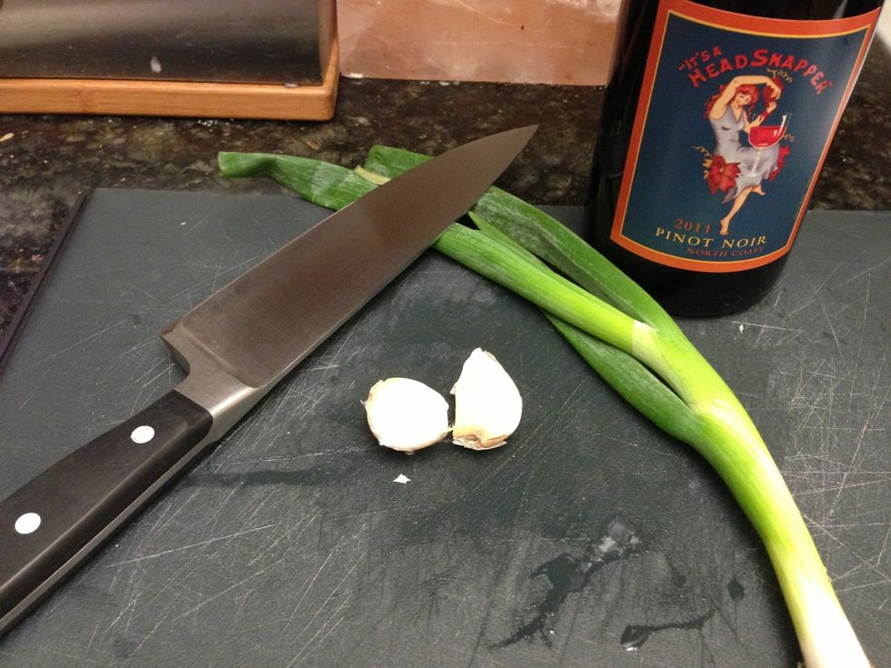 While the charcoal is heating let's start our red wine reduction. Peel and chop the garlic and chop the green onion.