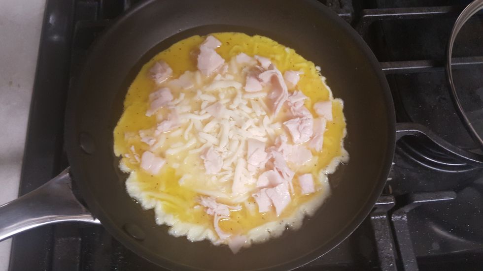 While the omelette is beginning to harden, add any extra ingredients you want. I added cheese and ham to mine, but you can add whatever ingredients you'd like.