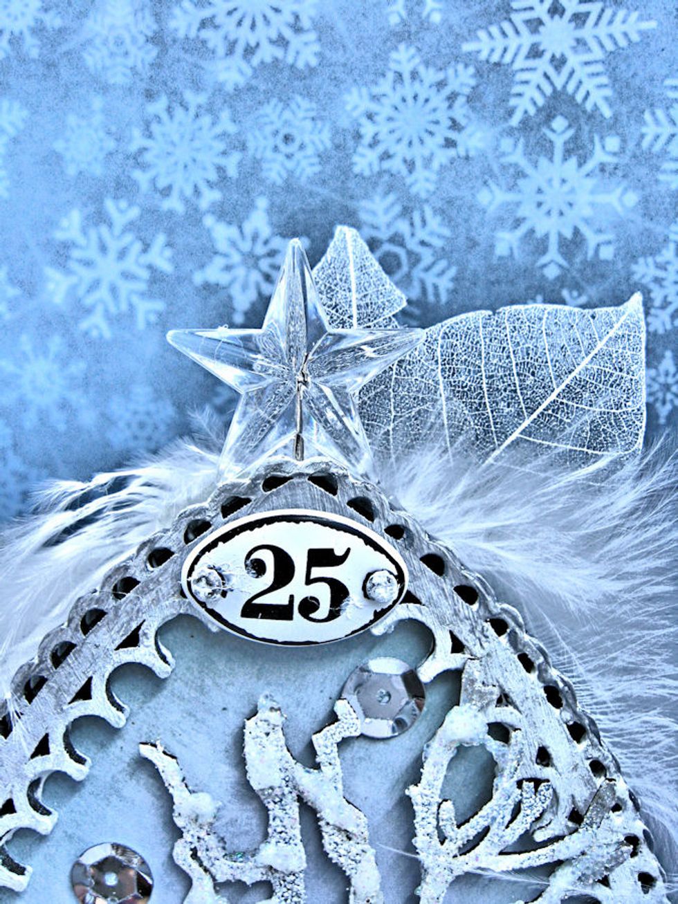 While the tree is drying in place, insert stick pin into the back of the frame.  Glue white feathers and skeleton leaves in place. Add screw brads to the mini plaquette and glue in place.