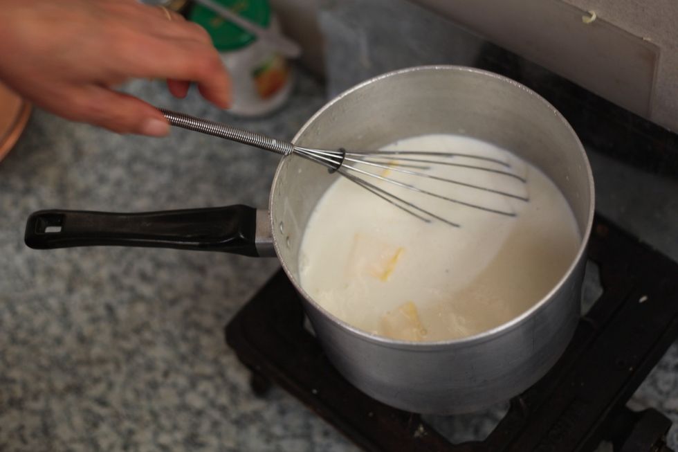 While you're heating up the milk and four tablespoons of plain flour, add 2 large tablespoons of butter and 1 tablespoon of vege stock. Keep stirring with a whisk. Let's not burn the milk. Stir stir..