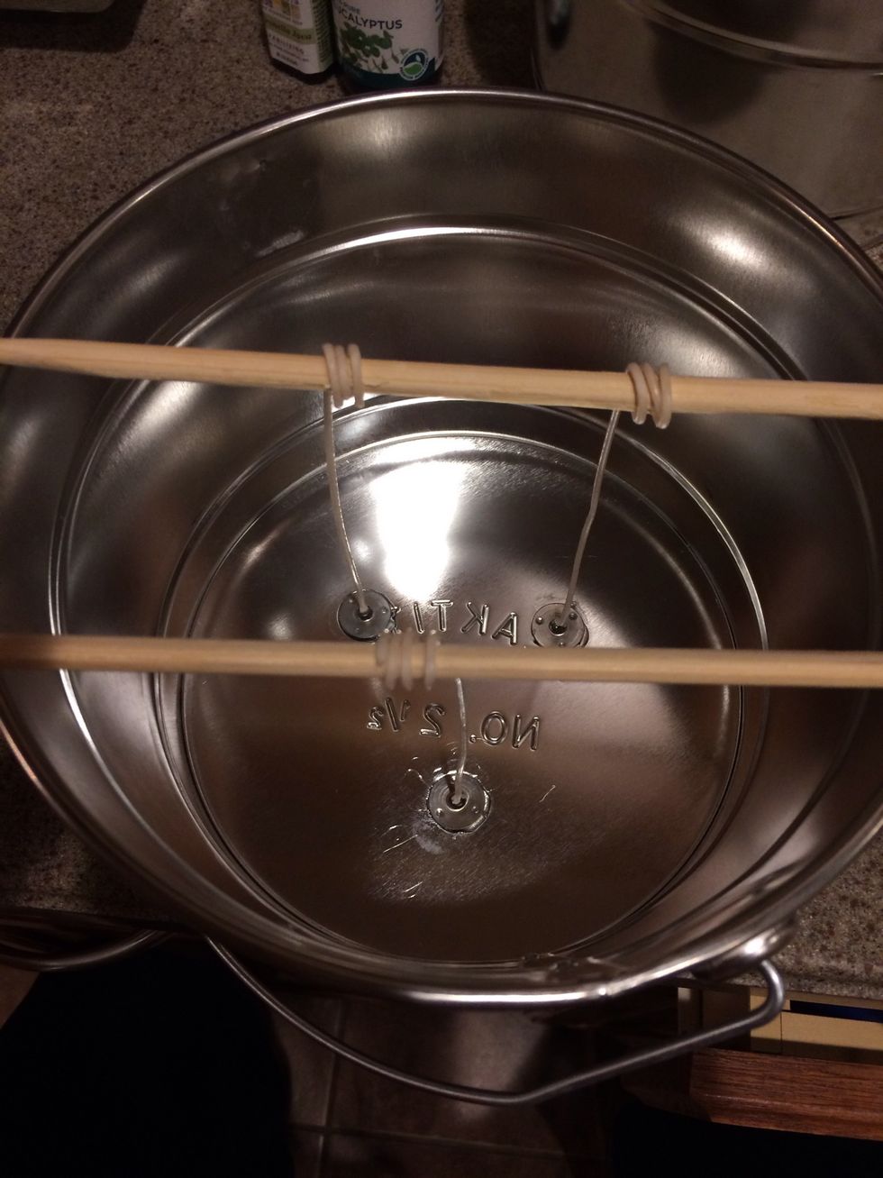 Wind wicks around chopsticks. This will hold them in place while you're pouring the wax into the tin pail.