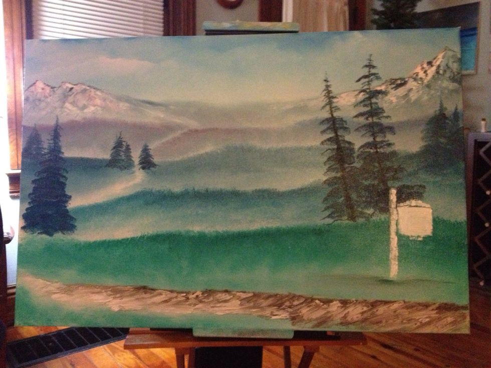 With a fan brush, add pine trees by starting at the top and tapping down. You can also add trunks if you wish with brown on a knife. The foreground road is knifed with brown then white.