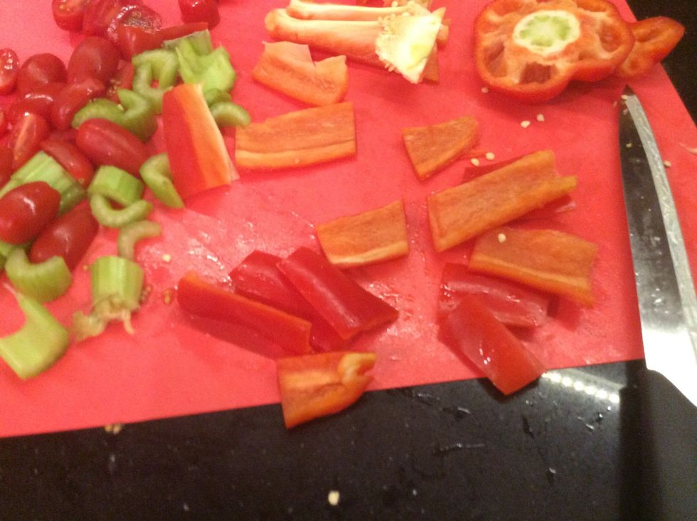 With a knife start to cut the celery sticks into little pieces the cherry tomatoes in half and the capsicum into strips